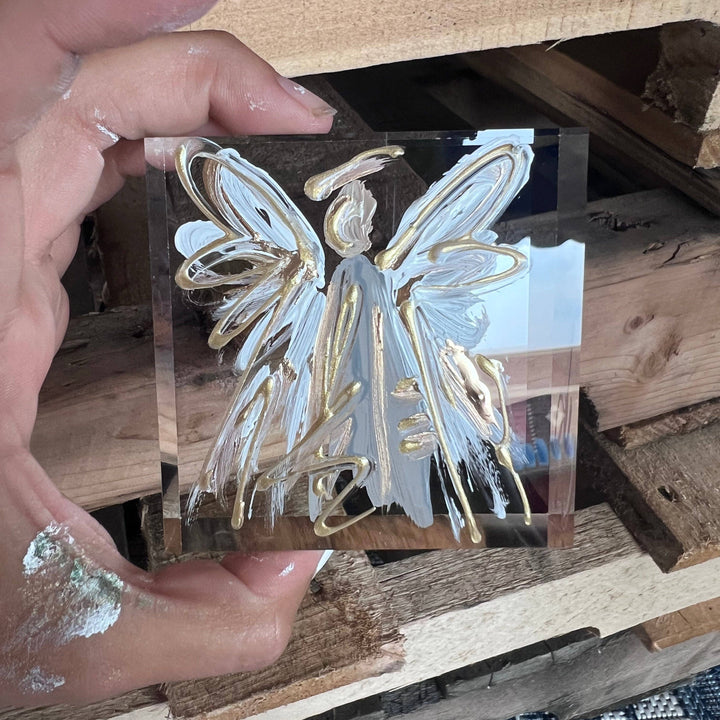 Hand holding a clear acrylic block with blue and gold angel design.