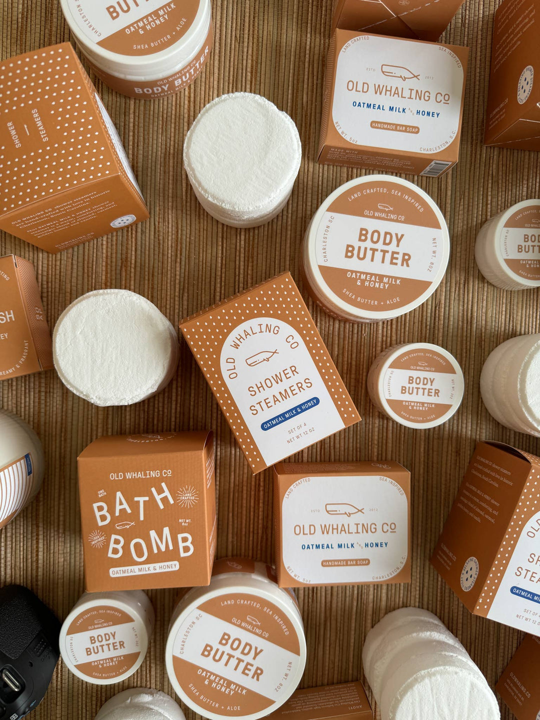 Collection of Old Whaling Co. bath products including body butters, shower steamers, and bath bombs on a wooden surface.