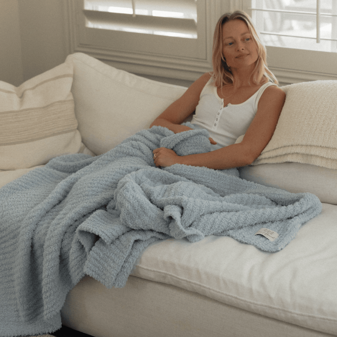 Woman sitting on a couch with a blue blanket, looking relaxed.