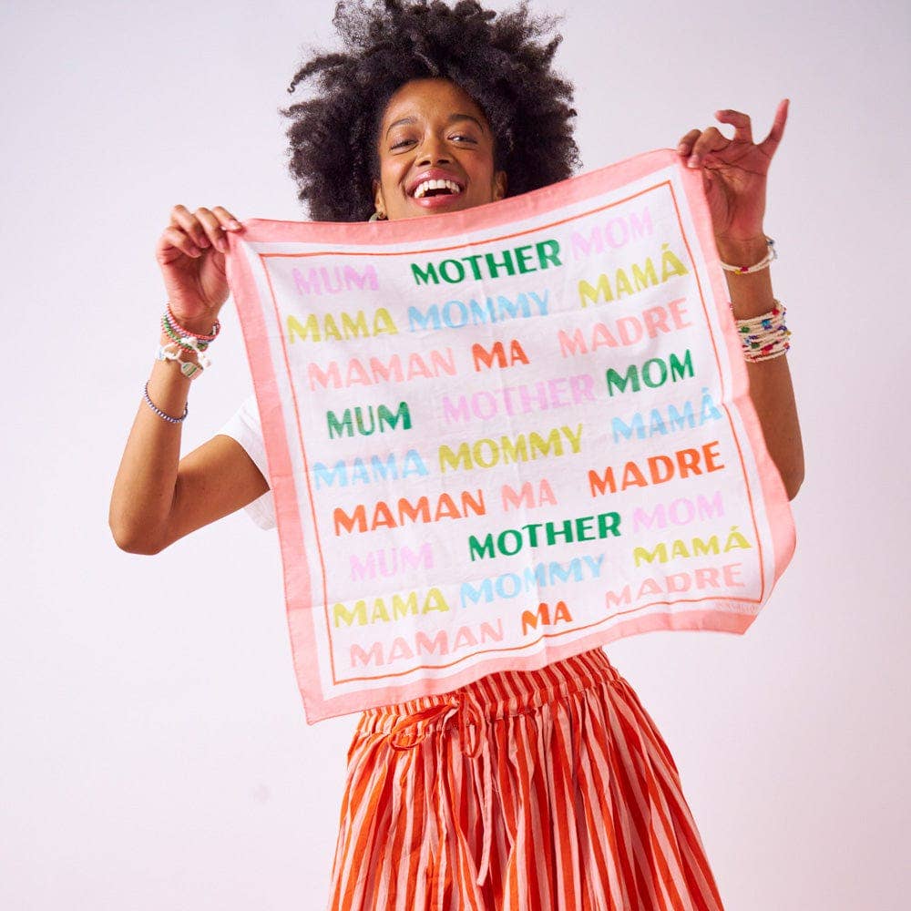 Woman holding a colorful towel with the word 'MAMA' in multiple languages.