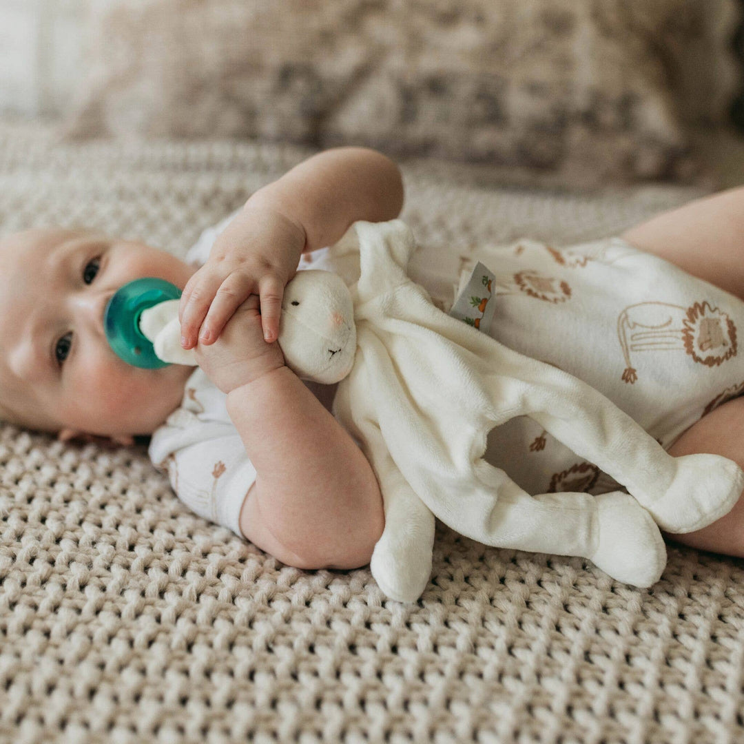 Baby lying on a textured surface with a teething toy and pacifier