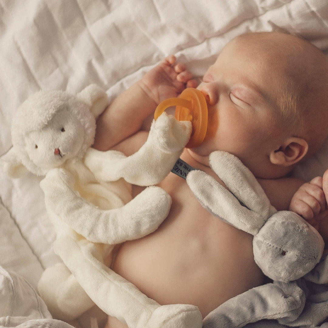 Baby sleeping with a white plush toy and orange pacifier on a soft surface