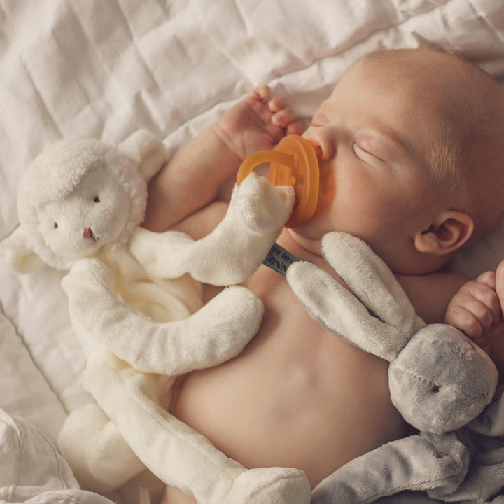 Baby sleeping with a white plush toy and orange pacifier on a soft surface