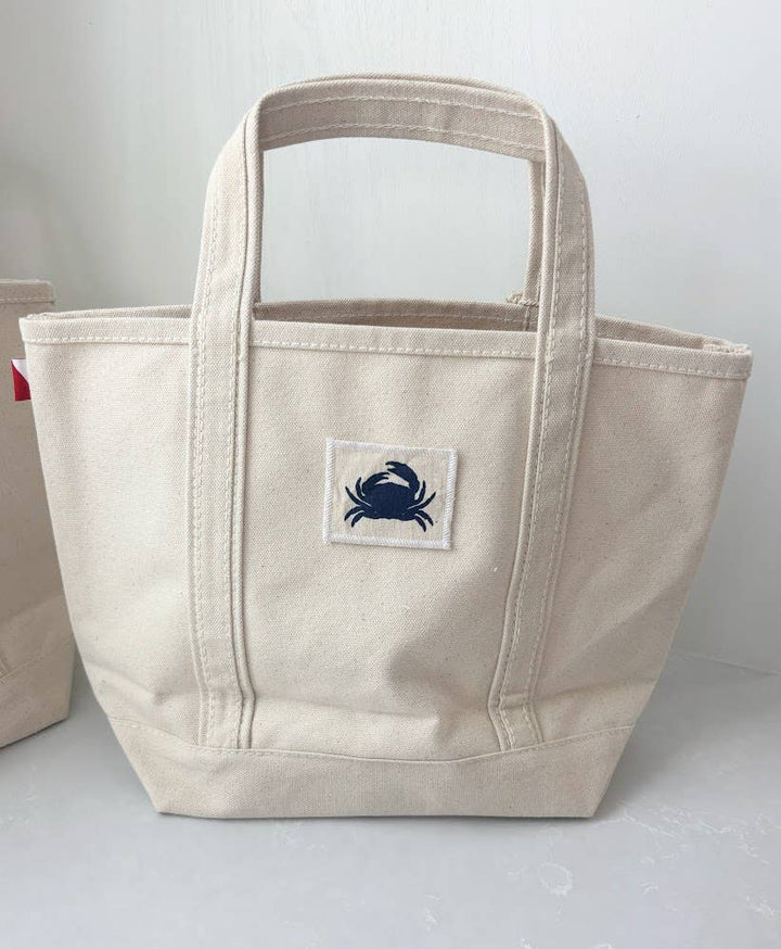 Beige tote bag with a blue crab logo on a white background