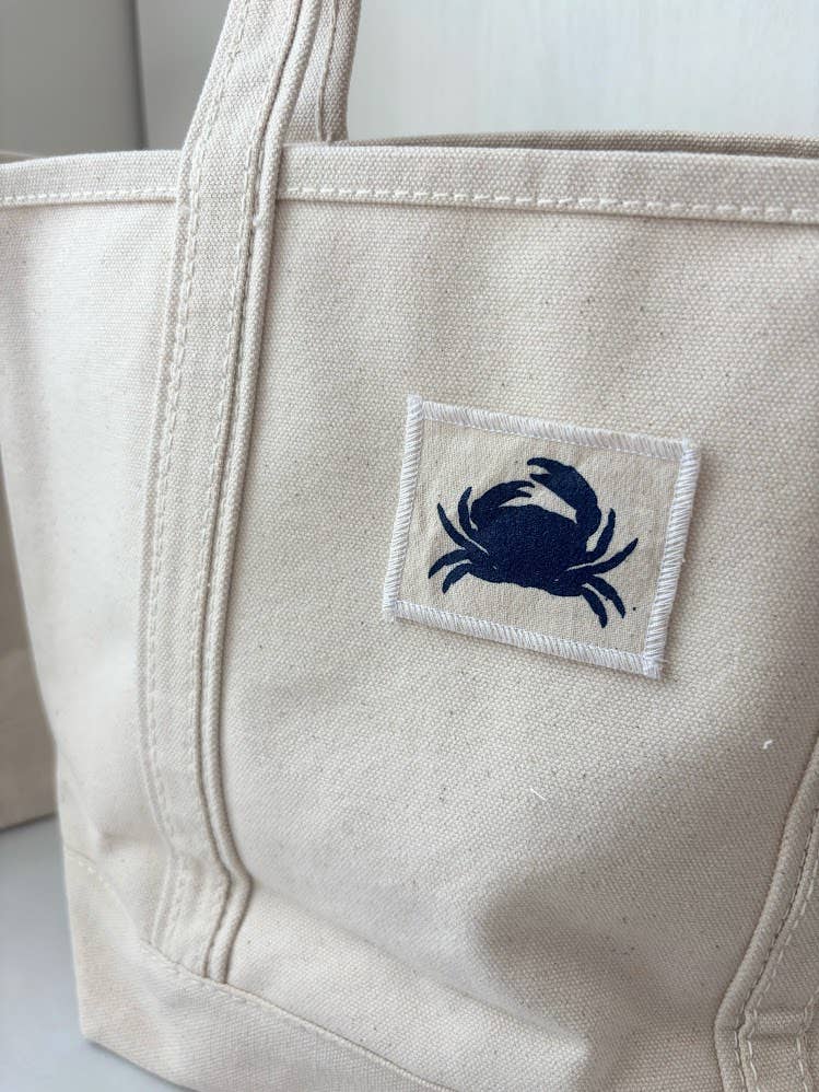 Beige tote bag with a blue crab patch on a light background