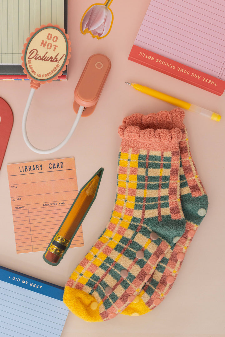 Plaid socks with a pen, library card, and notepad on a pink background