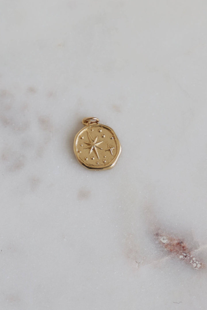 Gold compass pendant on a marble surface