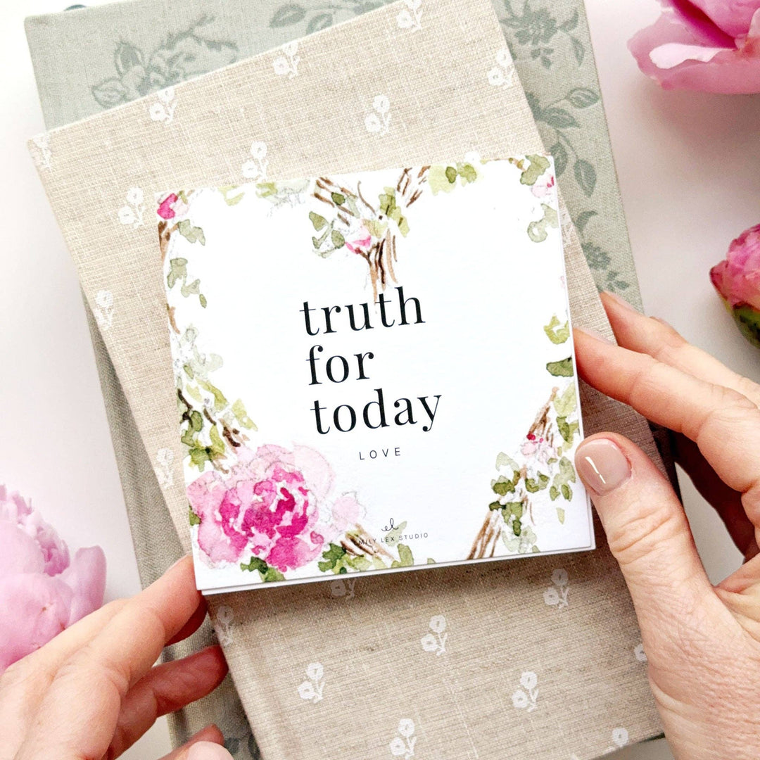 Card with 'truth for today' text and floral design held by hands on a textured surface with flowers.