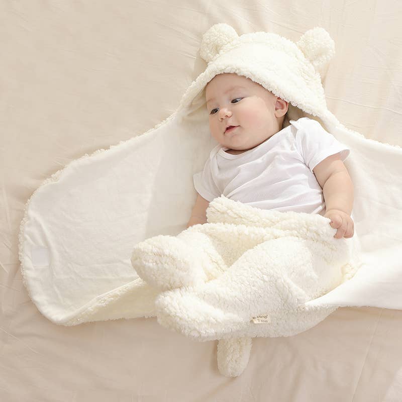 Baby wrapped in a white fluffy swaddle with bear ears on a beige background