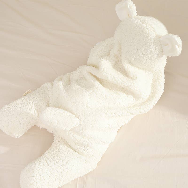 A plush teddy bear-shaped baby onesie in soft cream fleece, laid flat on a light beige fabric background.