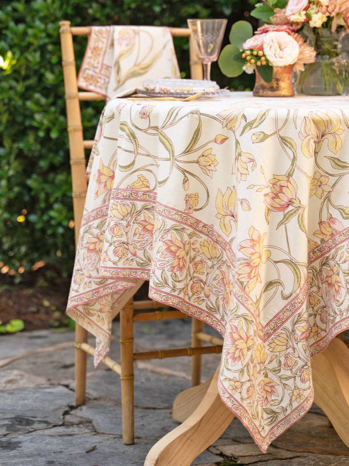 Floral-patterned tablecloth on a table outdoors with chairs and flowers.
