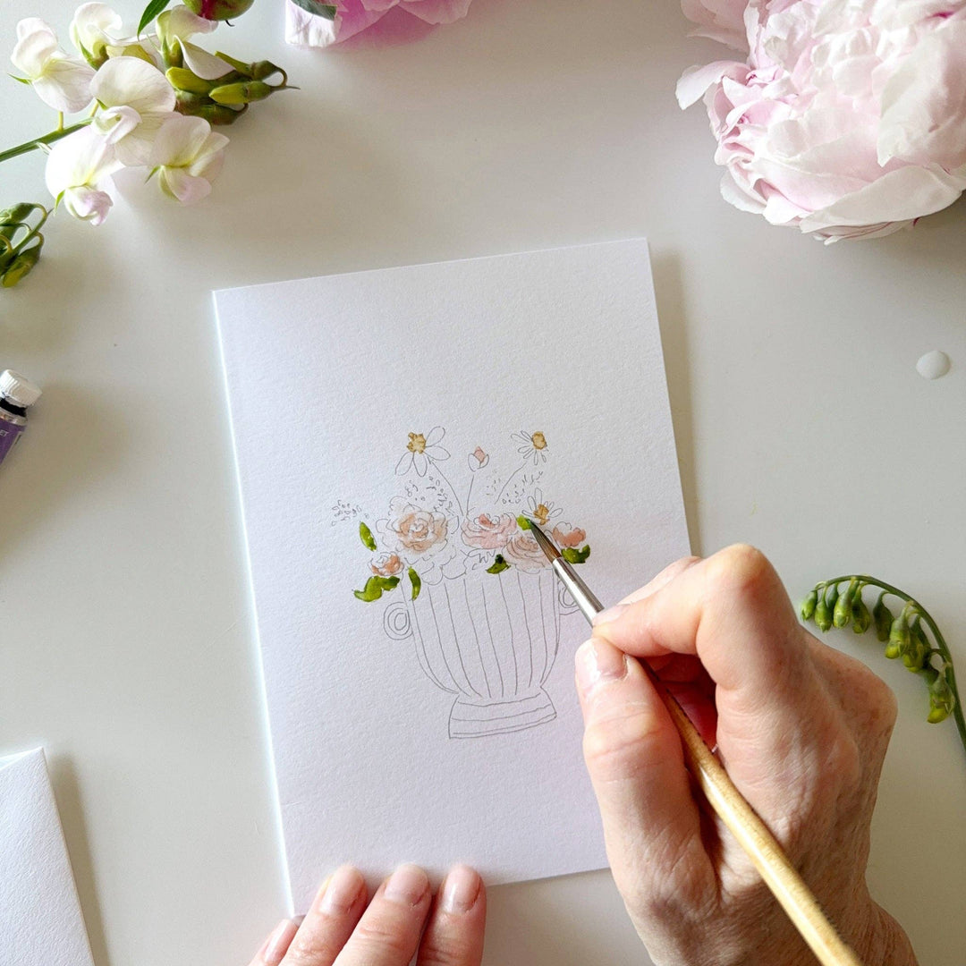 Person coloring a floral design on a card with flowers around
