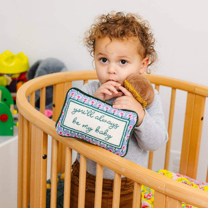Child in a crib holding a needlepoint pillow with a message