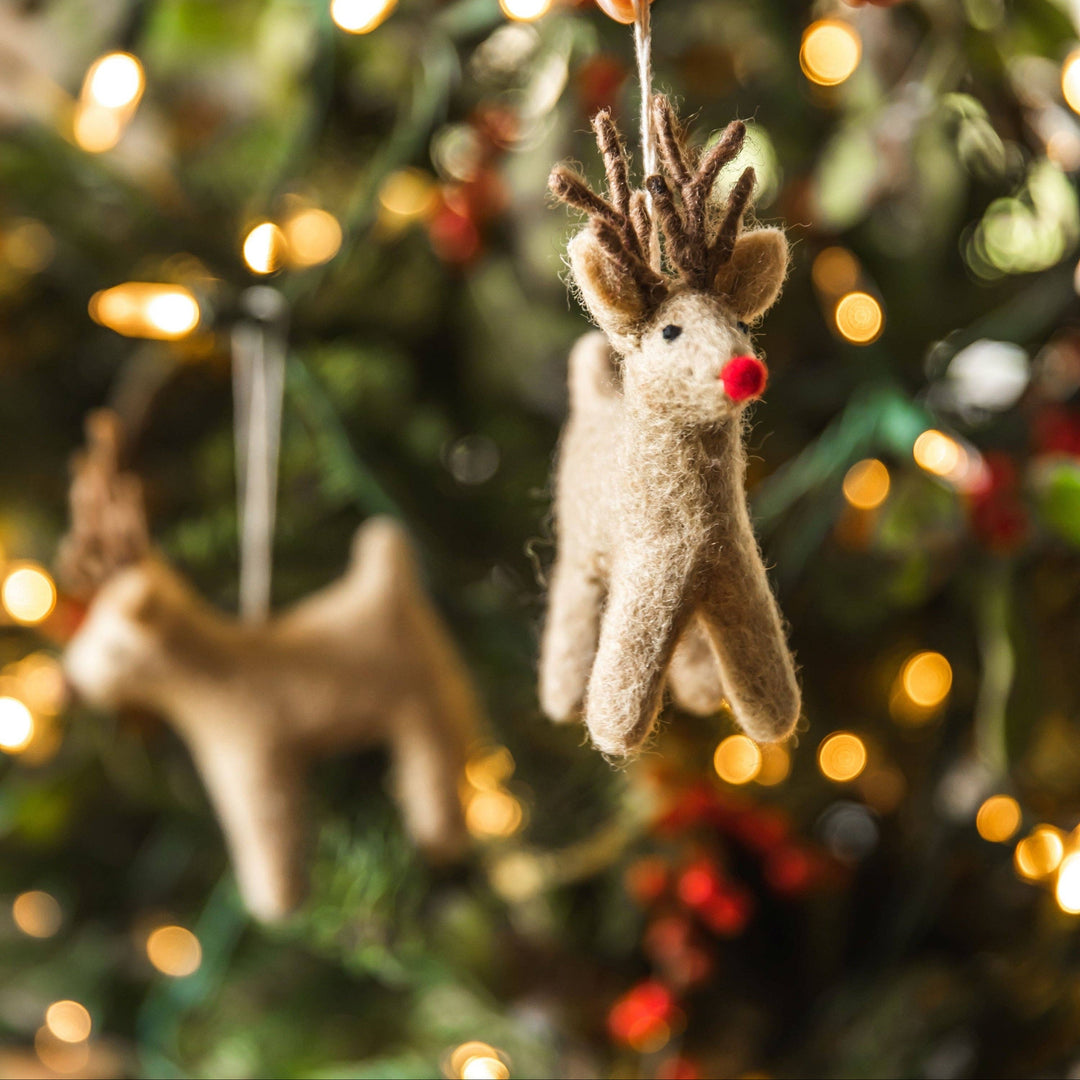 Hand holding a small reindeer ornament against a blurred Christmas tree background.