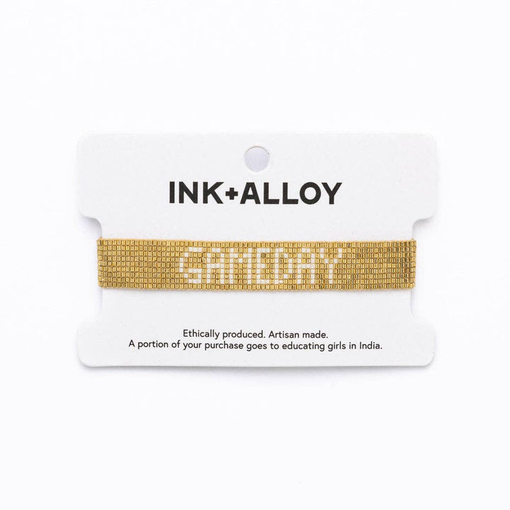 Gold bracelet on a white card with 'INK+ALLOY' branding