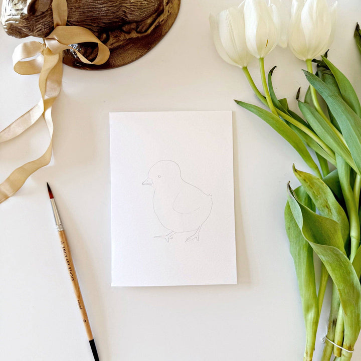 White paper with a pencil drawing, white tulips, and a brown hat on a light surface.