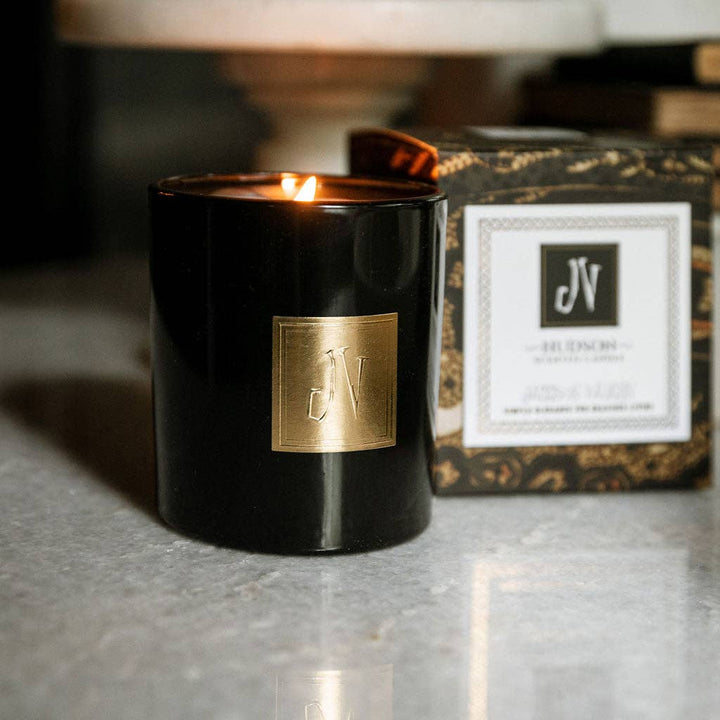 Black candle with gold logo and packaging in the background