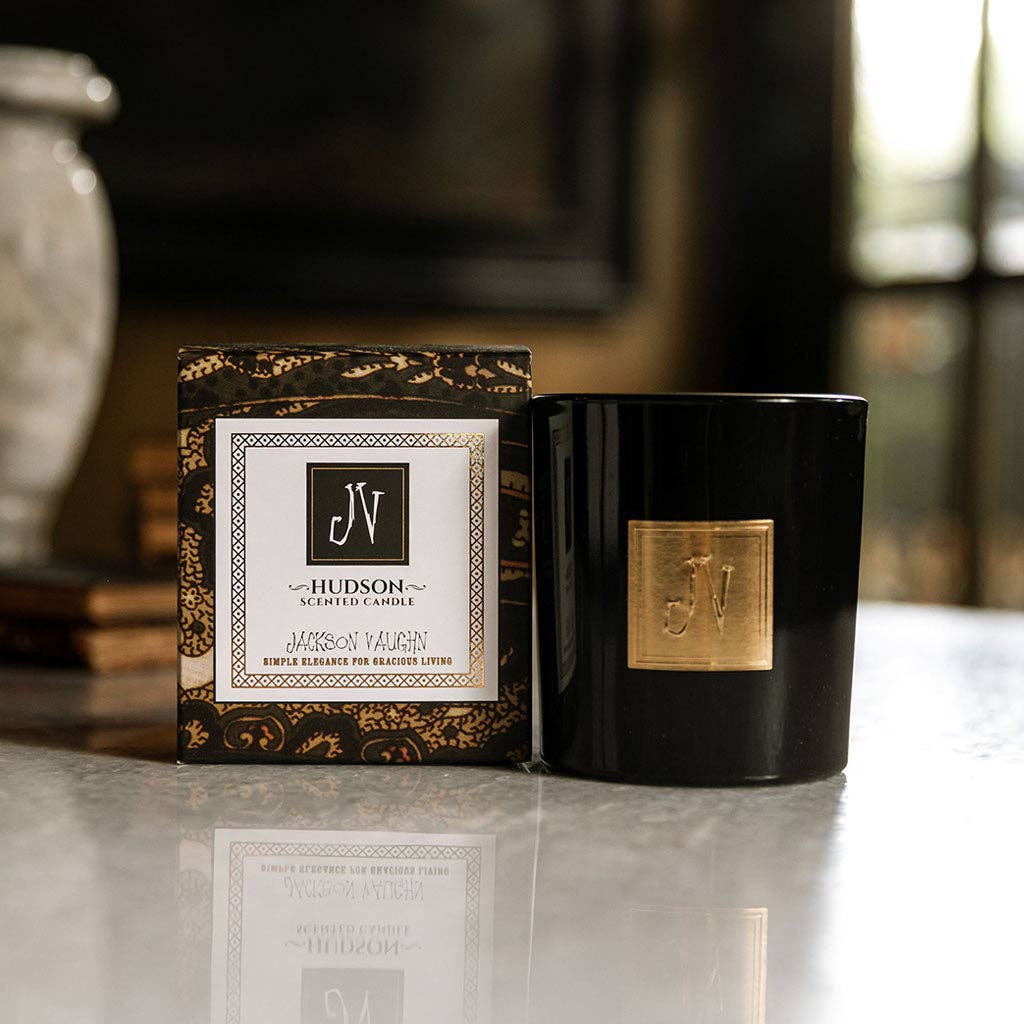 Black candle with gold accents and packaging on a reflective surface