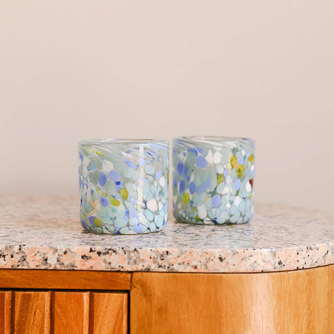 Two blue mosaic drinking glasses on a countertop with a neutral background