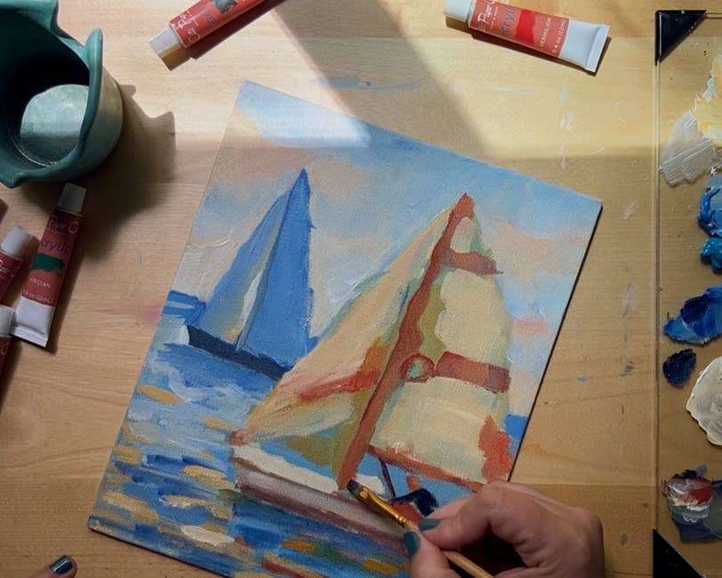Painting of sailboats on a wooden surface with art supplies.
