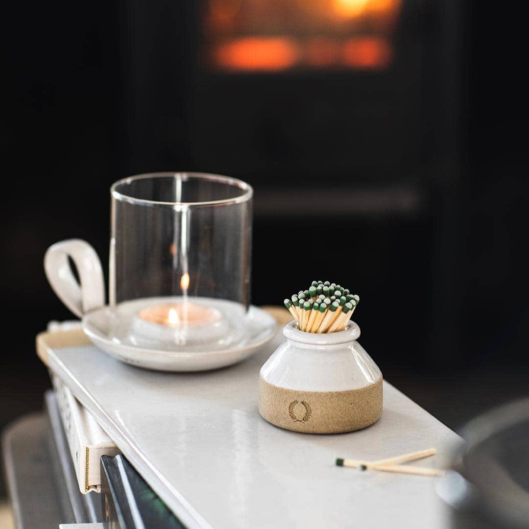 Milk Bottle Match Striker with a votive candle and glass container and two matches on a tray with a fireplace in the background