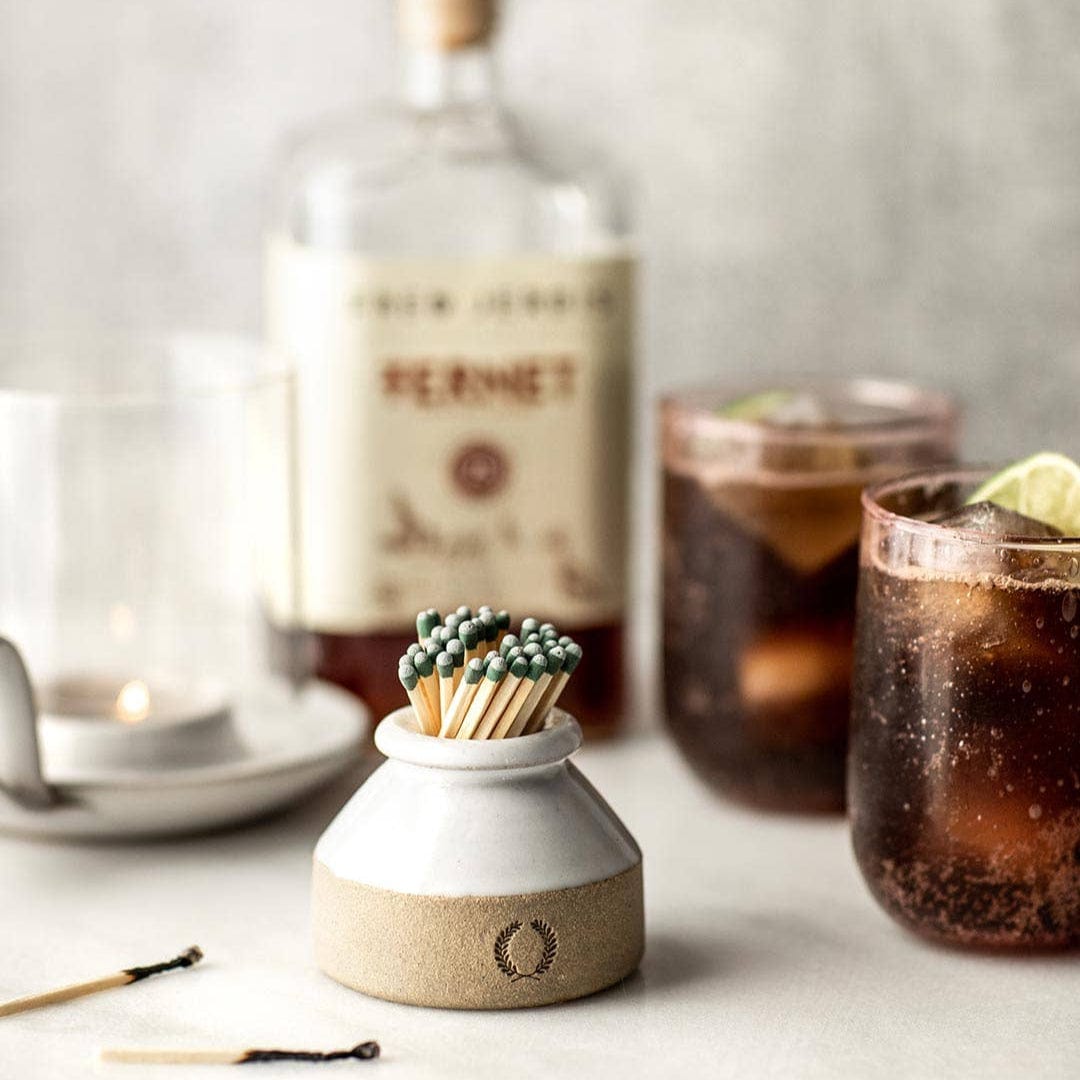 Milk Bottle Match Striker filled with green-tipped matches and two glasses of soda and a lime with a bottle of Peronet in the background. 