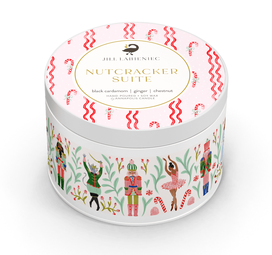 A round white candle tin with a festive holiday label reading 'JHL LABENIEC NUTCRACKER SUITE' on the lid, decorated with red candy canes, green holly, and nutcracker figures on a white background.