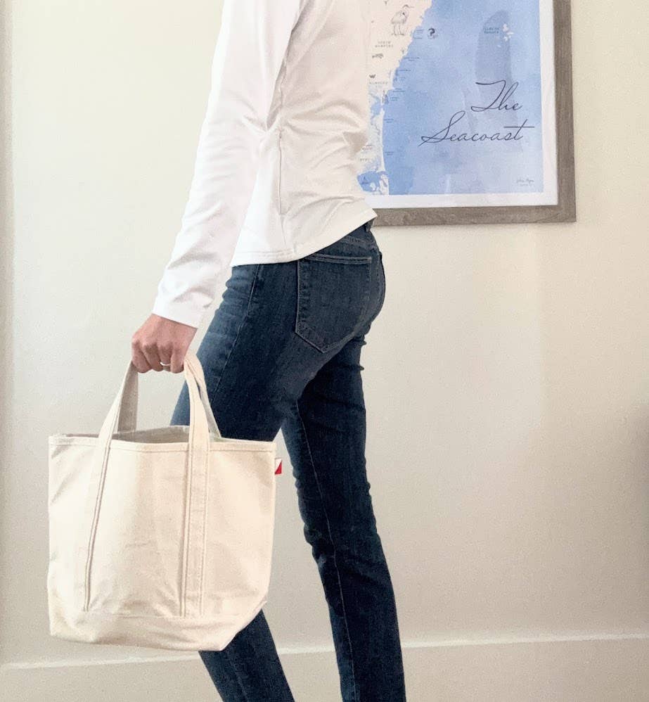 Person holding a beige tote bag in a room with a framed picture on the wall.