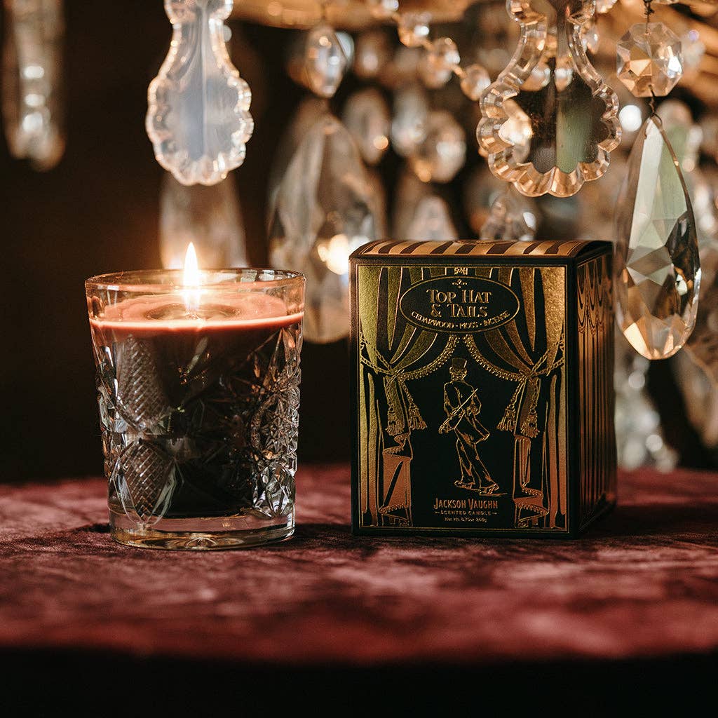 Candle in a glass holder next to a decorative box with intricate designs, set against a blurred background of hanging crystals.