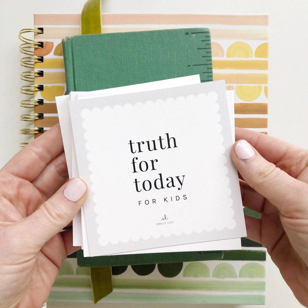 A person holds a stack of white cards with the text 'truth for today FOR KIDS' in black lettering, with a green notebook and patterned stationery in the background.