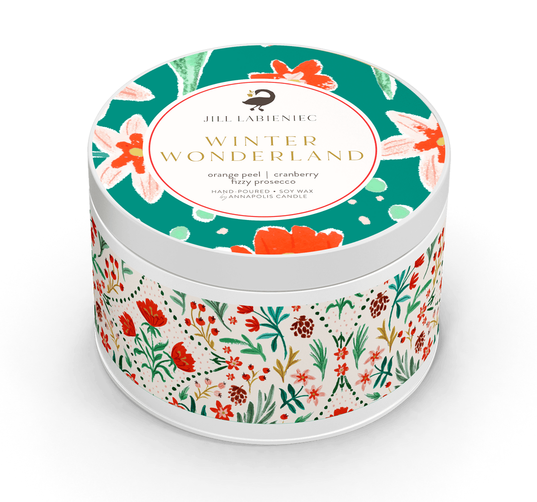 A round metal tin candle labeled 'Winter Wonderland' by Jill Lareniec, featuring a teal lid with floral illustrations and a white body wrapped in a red, green, and white botanical pattern, shown on a white background.